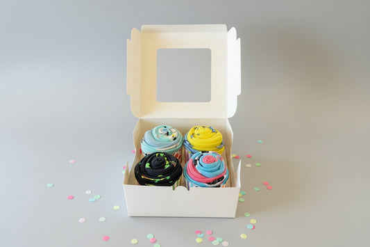 4 food themed sock cupcakes in a box on a dark surface
