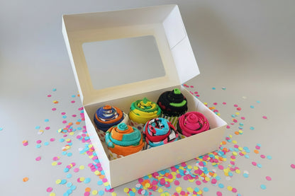 Box of colorful sock cupcakes with a window on top, surrounded by confetti on a light background