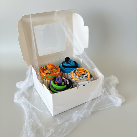 Four rolled halloween socks arranged in a white gift box with a clear window lid, set on a dark surface.