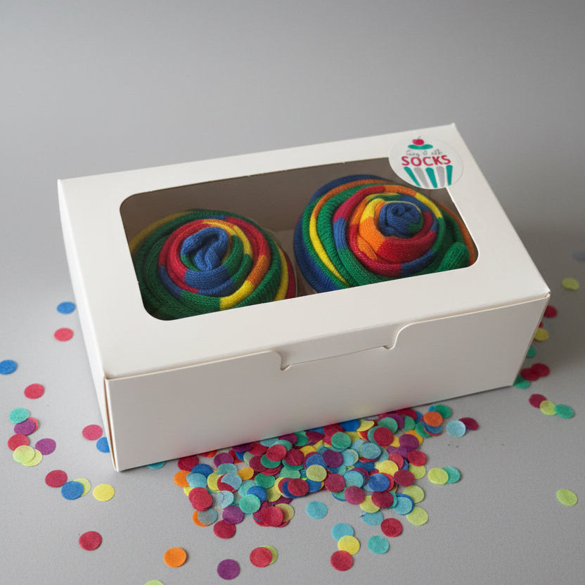 Colorful cupcake socks in a white box with a brand logo on a reflective surface.