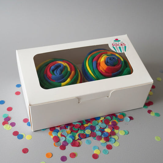 Colorful cupcake socks in a white box with a brand logo on a reflective surface.