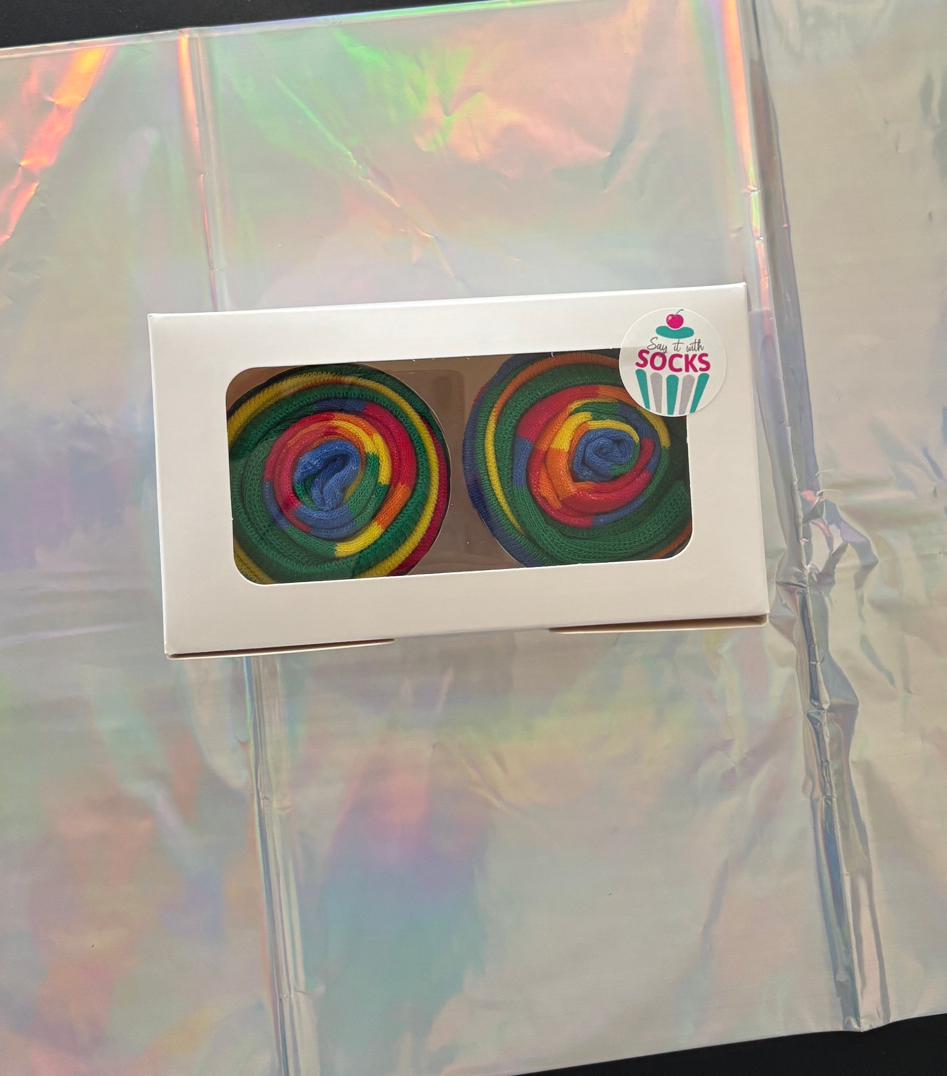 Pair of rainbow-patterned socks in a box on a reflective surface