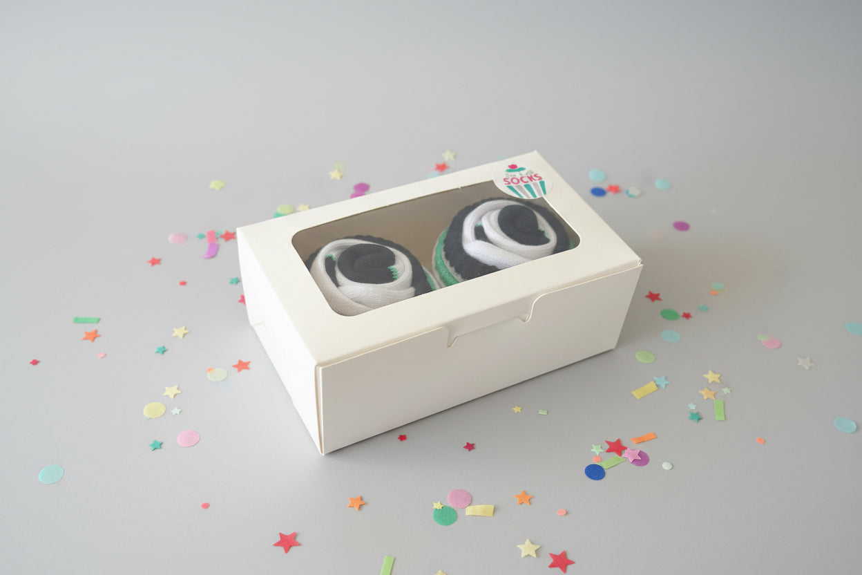 Two pairs of cupcake socks in a box with a visible brand logo on a dark background