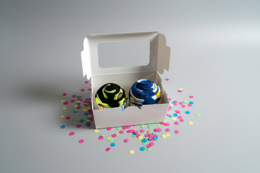 Two pairs of socks rolled like cupcakes in a white box on a wooden surface